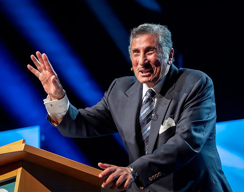 Dr. Youssef smiling and gesturing, speaking onstage at a podium