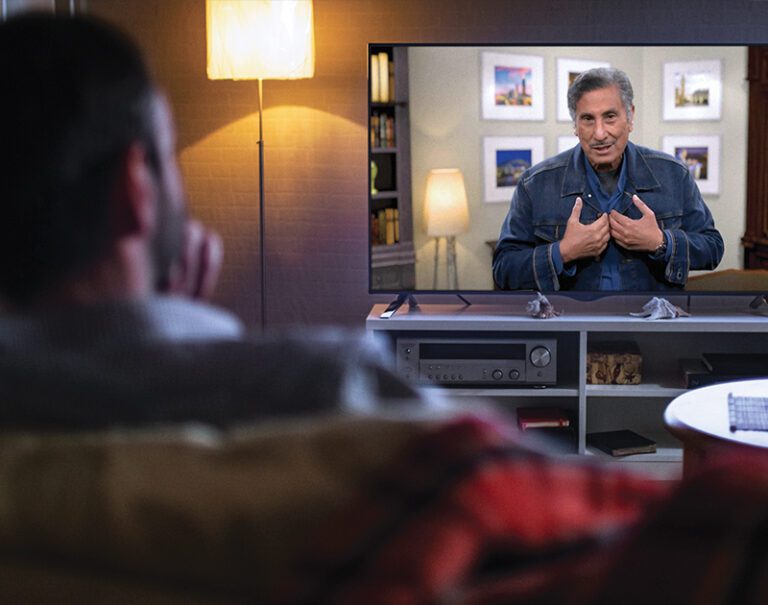 photo of the back of a man's head watching Dr. Youssef on a television in a living room