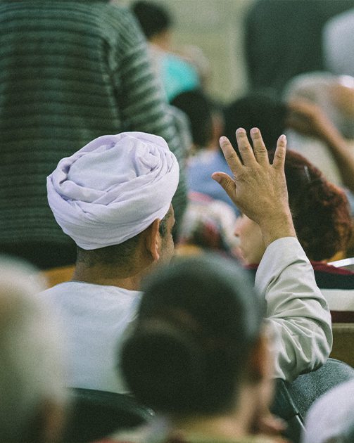 a behind shot of a man in a turban raising his hand in a religious service