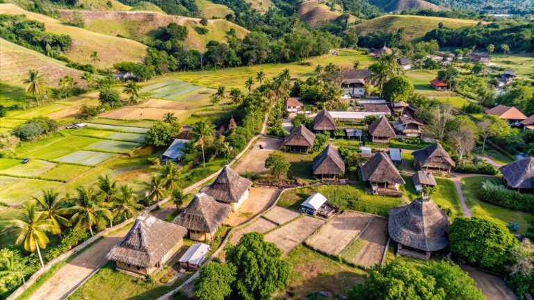 Aerial shot of village with straw roofs, rolling hills, and trees