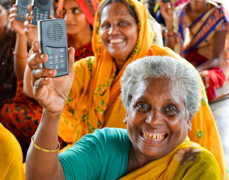 two older women in colorful garb smiling and holding Leading the Way audio recorders